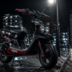 scooter booster garé sur bitume mouillé la nuit
