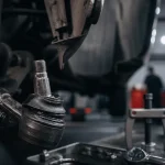 Rotule de direction usée visible sur une roue avant, soufflet abîmé, jeu de direction, pneus usés
